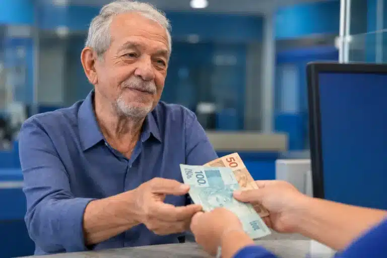 Idoso recebendo pagamento em agência do INSS, representando pagamentos no teto de R$ 8.475,55 liberados nesta semana.