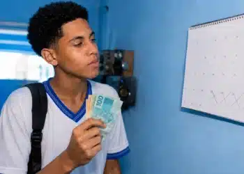 Estudante brasileiro conferindo o calendário e segurando dinheiro, ilustrando o depósito do benefício Pé-de-Meia em junho.
