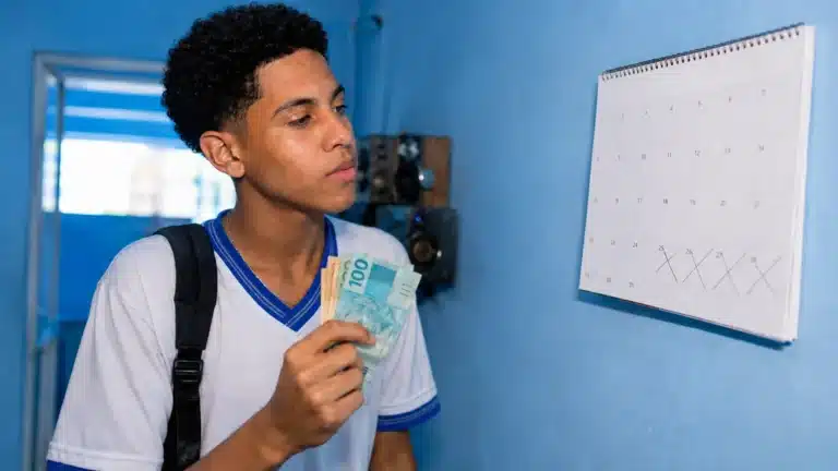 Estudante brasileiro conferindo o calendário e segurando dinheiro, ilustrando o depósito do benefício Pé-de-Meia em junho.