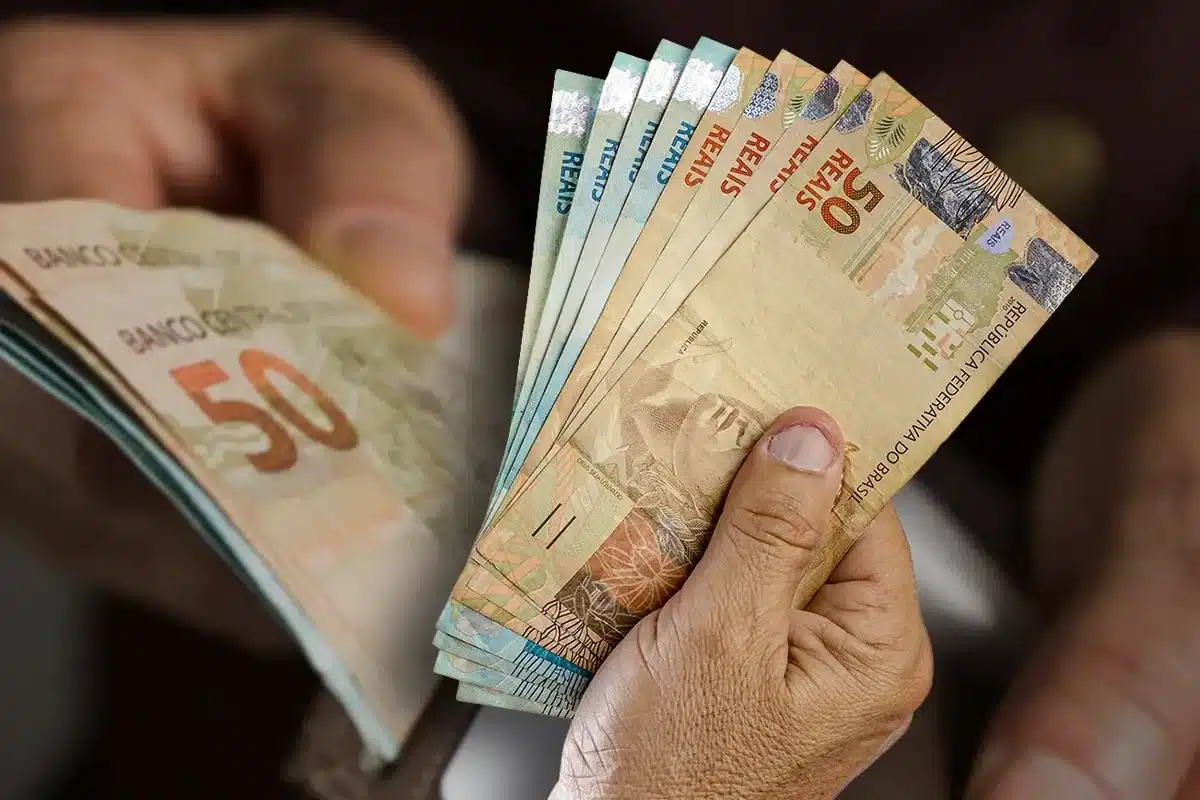 Mãos segurando cédulas de 50 reais, representando o Saque Calamidade de até R$ 6.220.