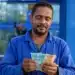 Trabalhador brasileiro conferindo notas de reais em frente a prédio bancário, representando o saque de R$ 6,2 mil do FGTS.
