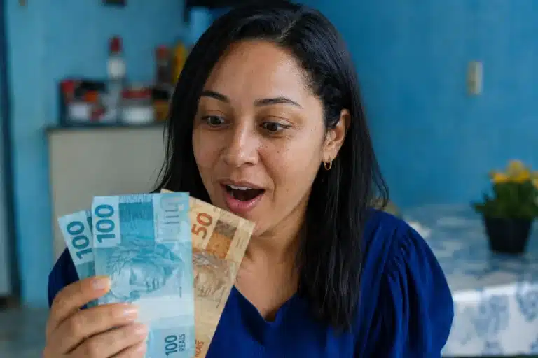 Mulher segurando notas de dinheiro, representando o saque do FGTS de até R$ 6.220 para moradores da BA, RJ e MG.